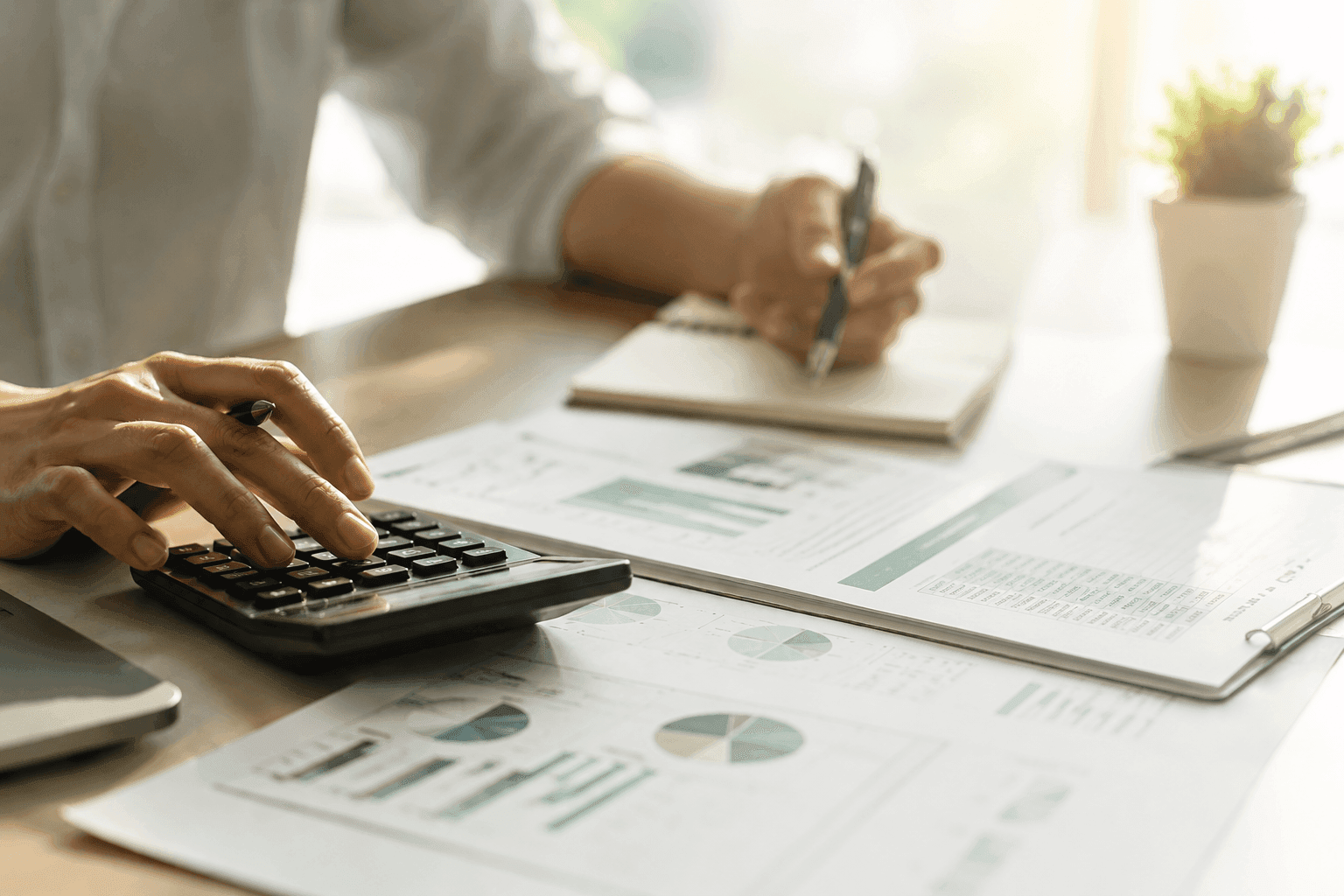 Close-up of hands reviewing financial reports and using a calculator